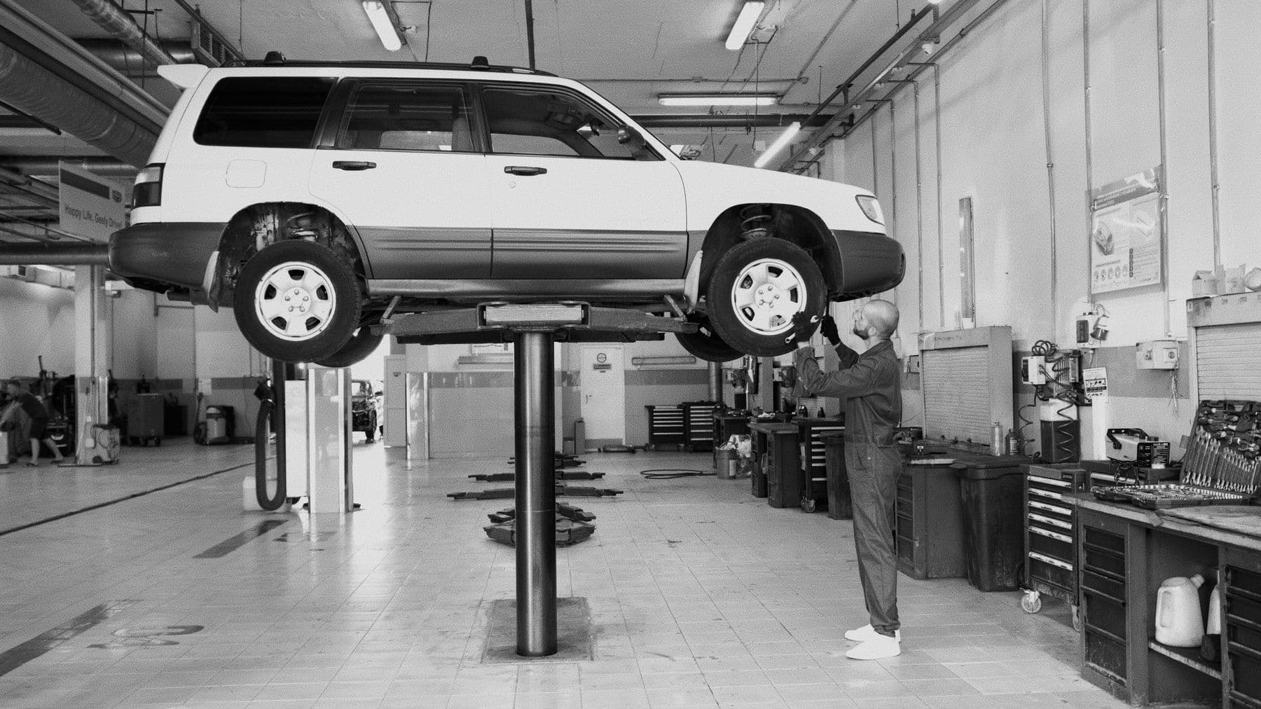 Monteur controleert een auto op een brug in een zwart-wit werkplaatsfoto